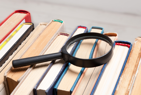 stack of books with magnifying glass to illustrate sources of information